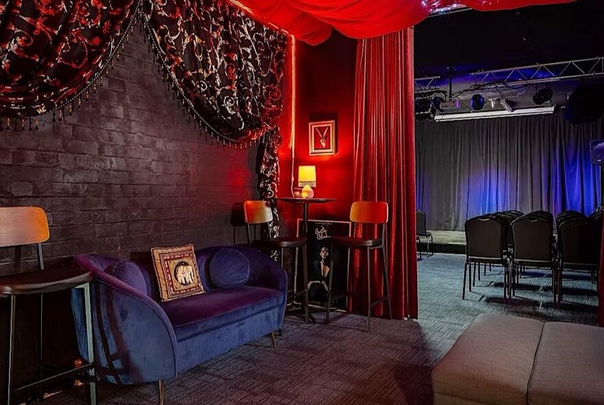 The upstairs bar and couch area of Voltaire, with a small stage and seats visible behind a heavy red velvet curtain.