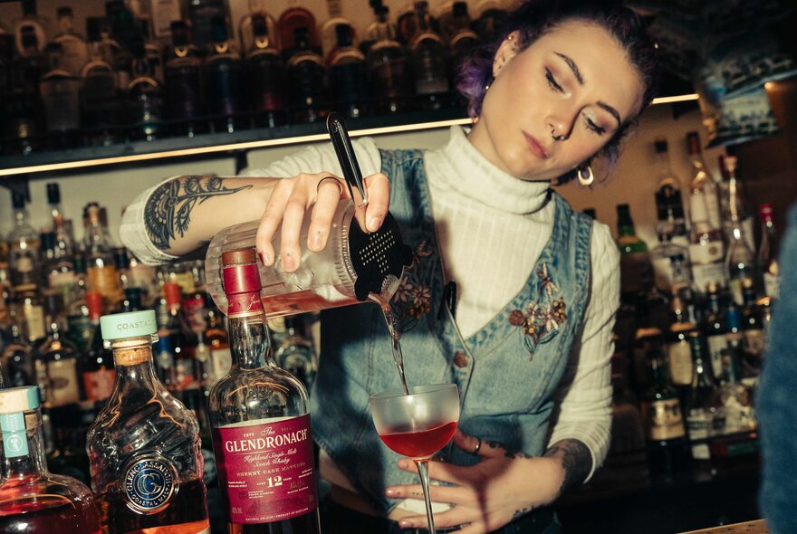 Bartender pouring a cocktail into a glass. 