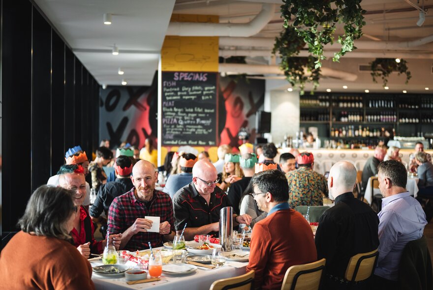 A packed dining room with large tables of families and friends enjoying a Christmas lunch. 