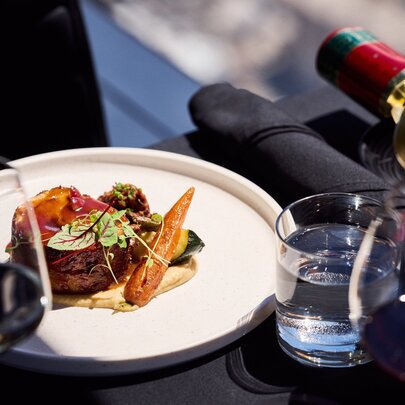 A fine dining steak and vegetable dish served with wine and water at a table in a restaurant.