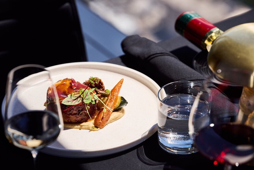 A fine dining steak and vegetable dish served with wine and water at a table in a restaurant.