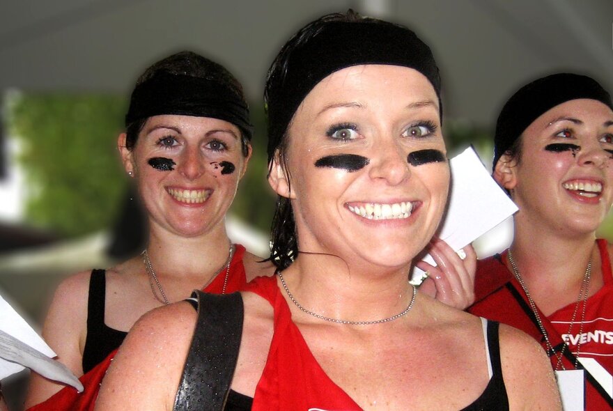 Three smiling people taking part in a challenge race, with black stripes on the cheeks on their faces.