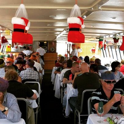 People wearing party hats seated at tables inside a cruise boat cabin decorated with Santa boots and other Christmas decorations.