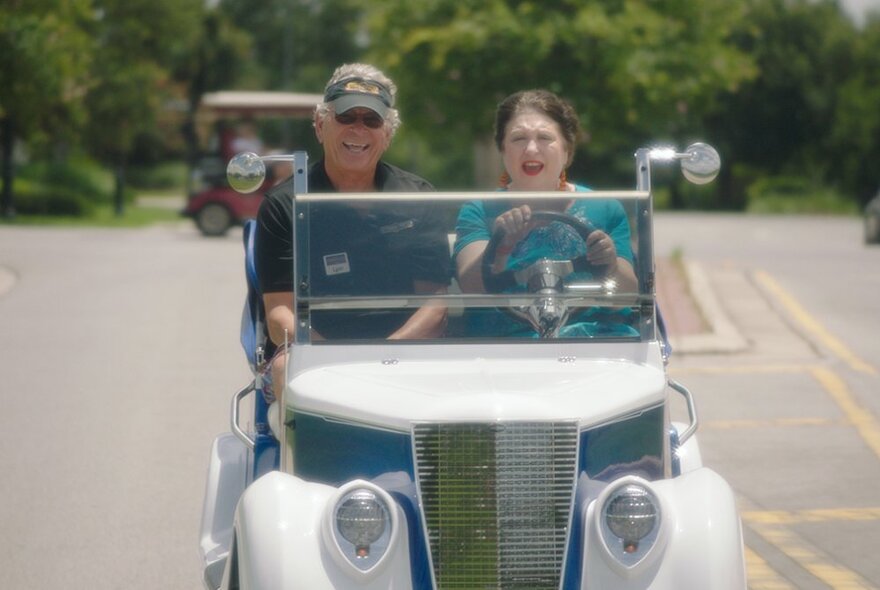 Two people in a small vintage car. 