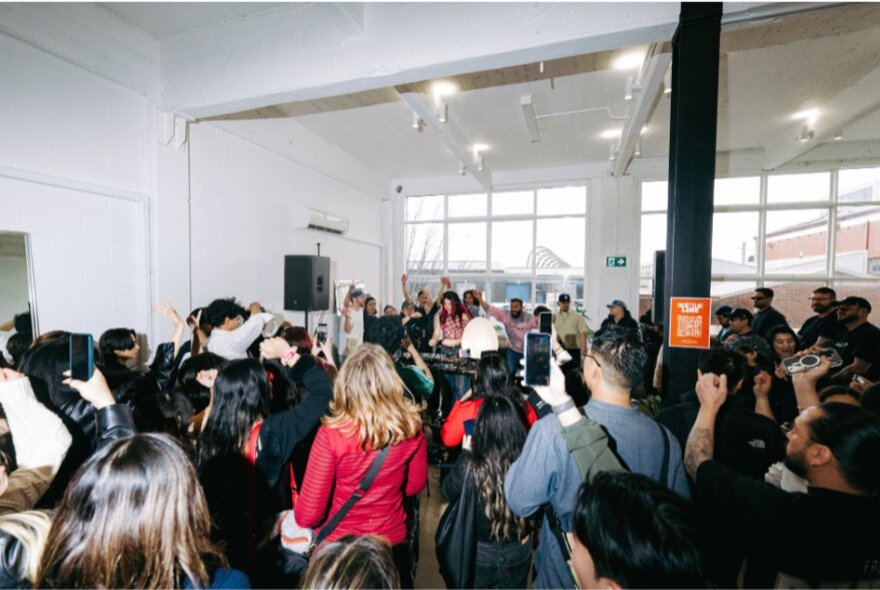 People dancing in an indoor space, daytime. some of them holding up their smart phones to film the room.