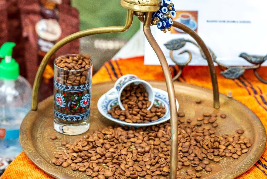 A brass tray with coffee beans, tea glass and cup and saucer.