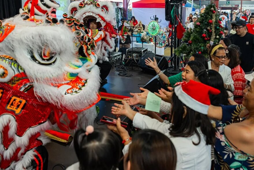 People wearing Santa hats reaching out to a red and white Filipino dragon puppet on stage.