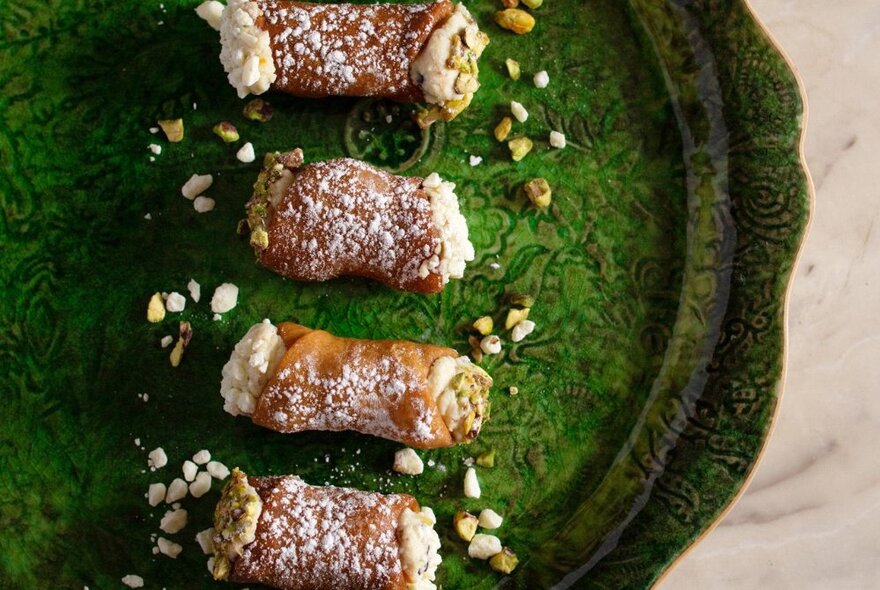 Looking down at ricotta filled cannoli or a green tray, garnished with pistachio nuts.