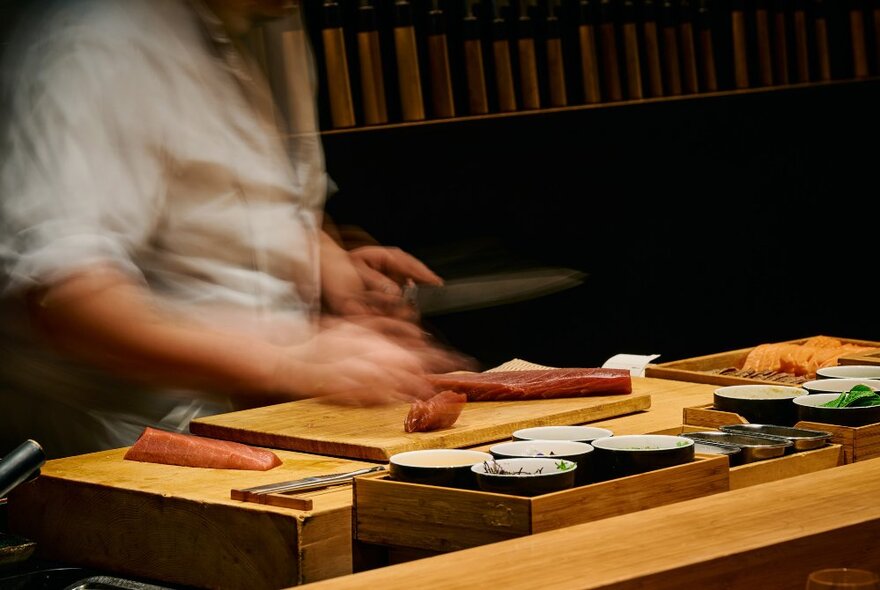 A sushi chef slicing tuna on a wooden board.