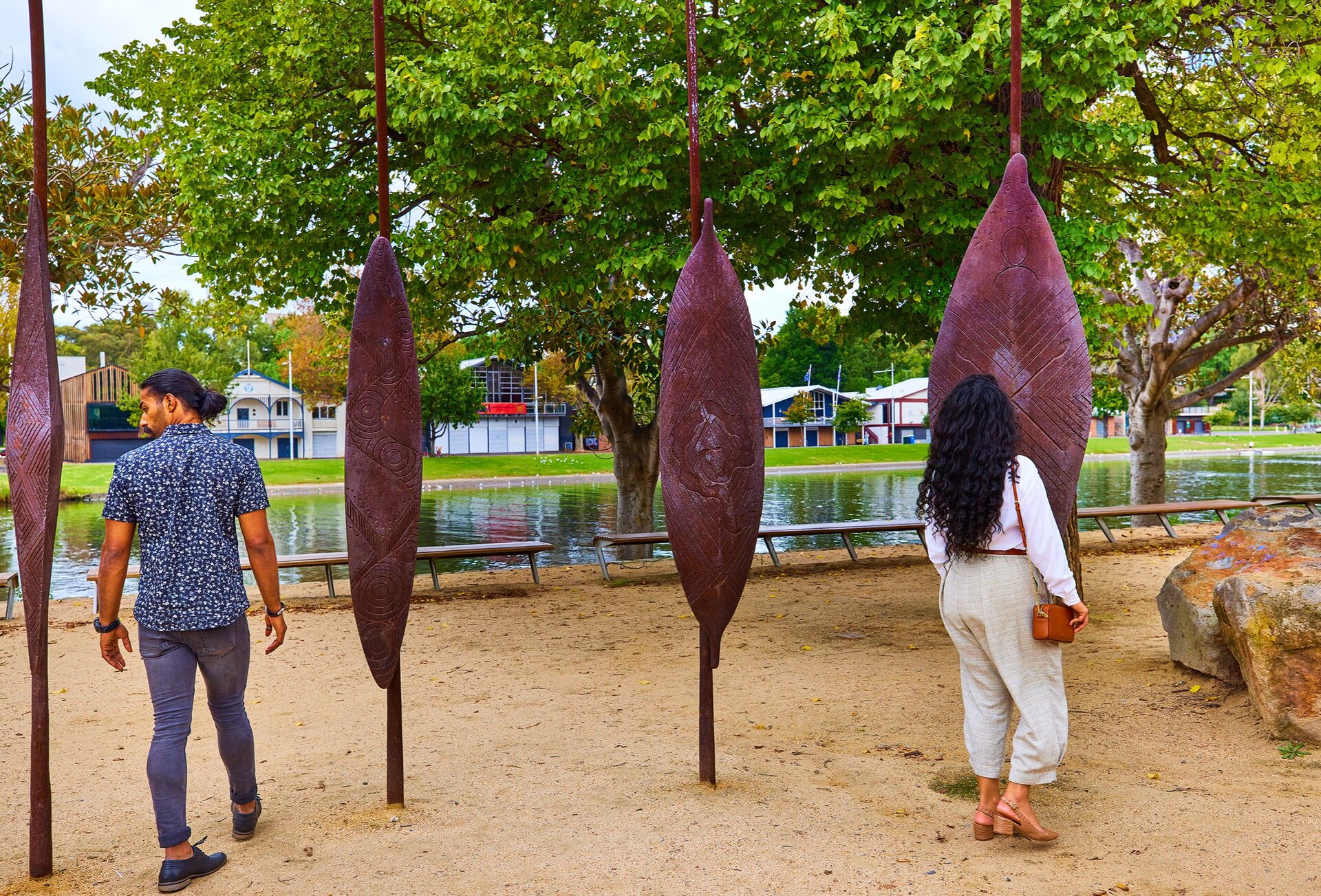 Two friends are looking at sculptures of Aboriginal shields placed along the banks of the Yarra River 