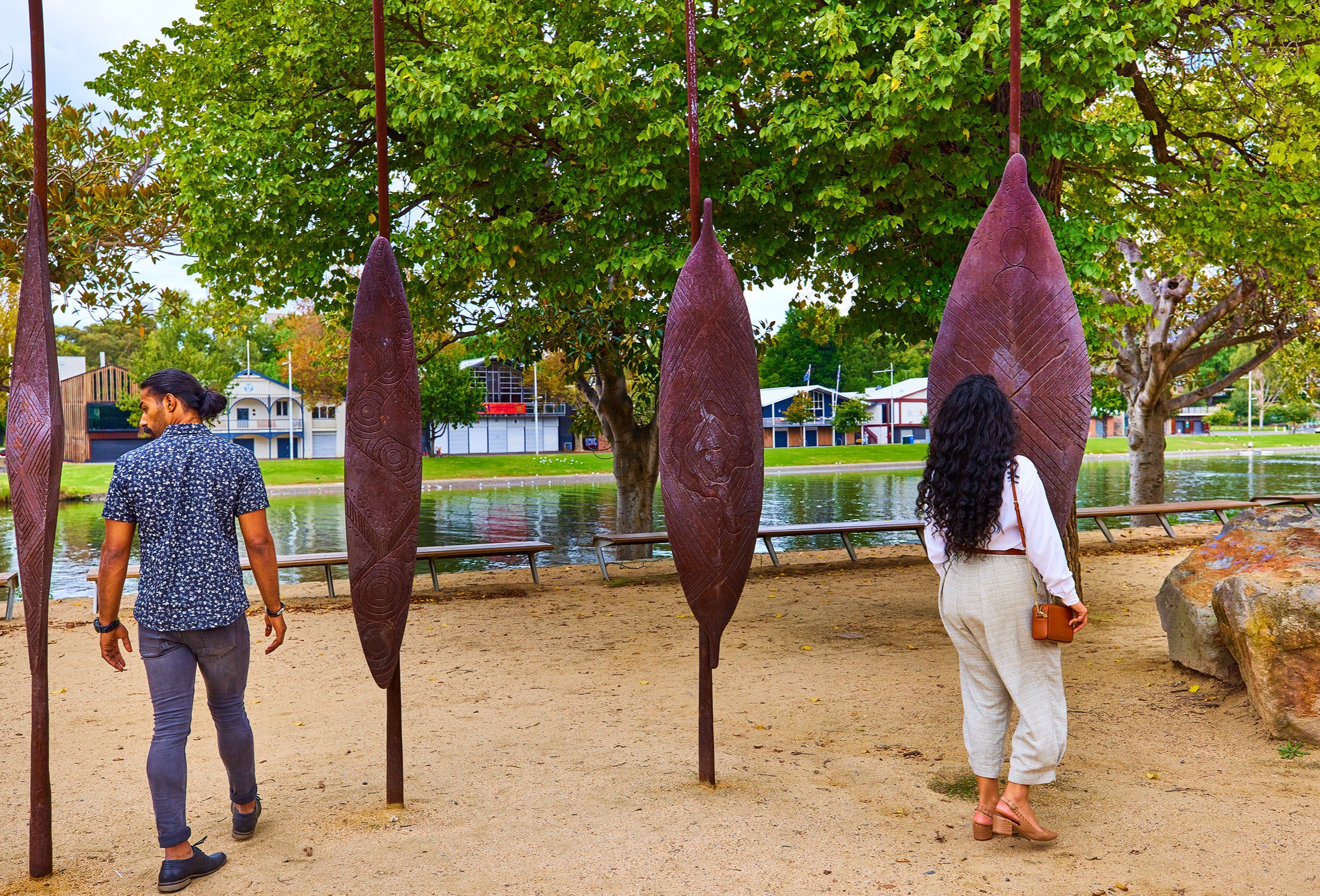 Two friends are looking at sculptures of Aboriginal shields placed along the banks of the Yarra River 