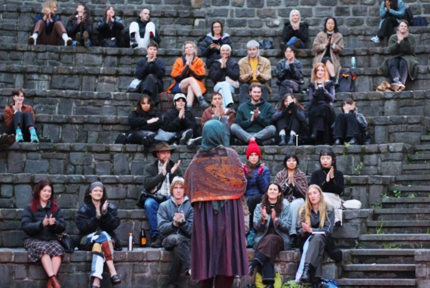 A crowd of people seated in an outdoor amphitheatre listening to a speaker.