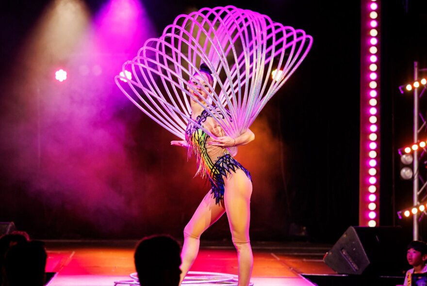 A circus performer with multiple hoola hoops, on stage at a children's show.