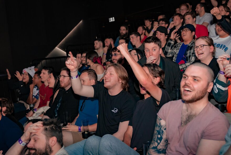 People seated in a theatre watching sport on a screen, some cheering. 