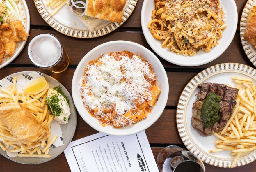 Looking down on a table with various plates of pasta and a glass of beer. 