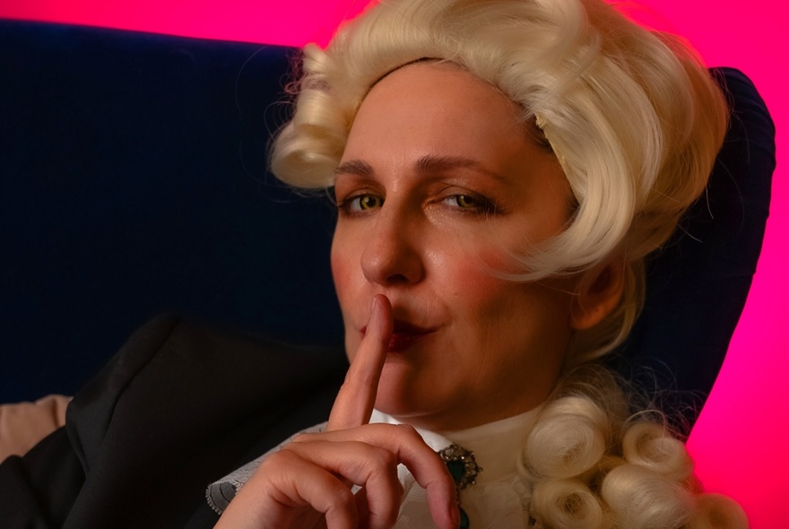 A woman dressed as a man in a powdered wig with her finger to her lips.