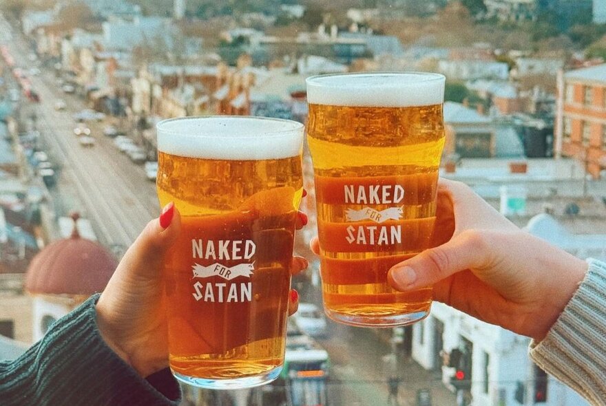 Two hands holding up beer glasses in front of the view of a Melbourne city street.
