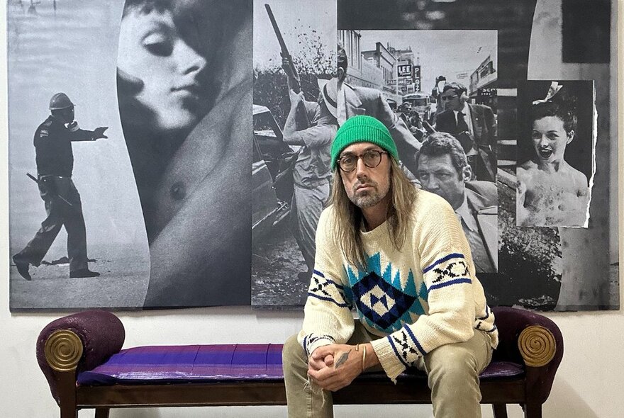 Artist seated in front of a collage artwork.
