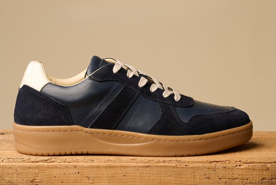Side view of a single black leather sneaker with tan sole and white laces. 