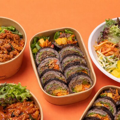A selection of Korean dishes in bowls and plates on an orange coloured table.