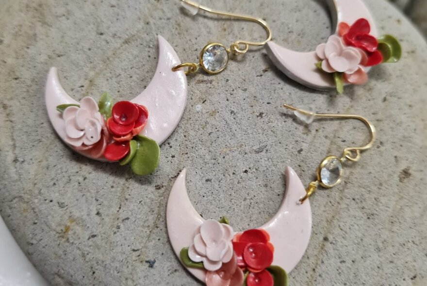 Earrings shaped like a crescent moon with a flower petal detail on them, made from polymer.