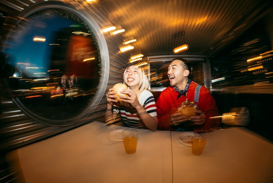 A blurred and distorted image of two young people eating burgers in a restaurant.