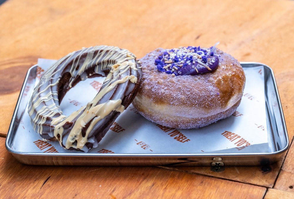 A cruller and an ube doughnut on a metal tray.