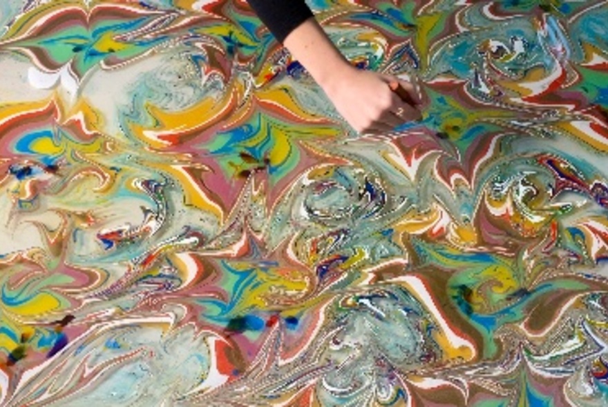 A person's hand performing water marbling with visible paint swirls. 