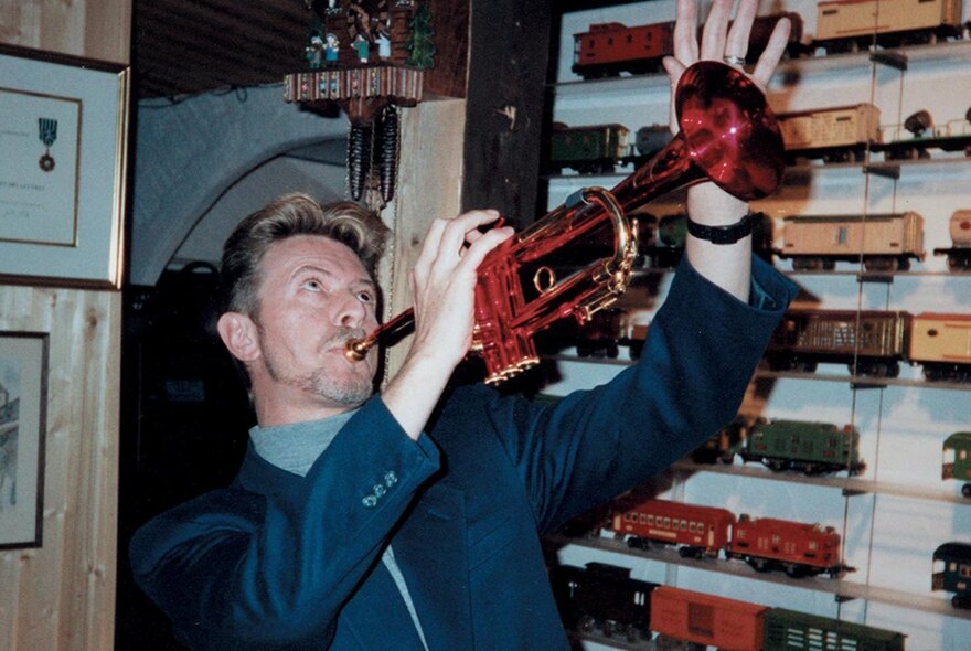 A man playing a red-tinted trumpet in front of a display of model trains.