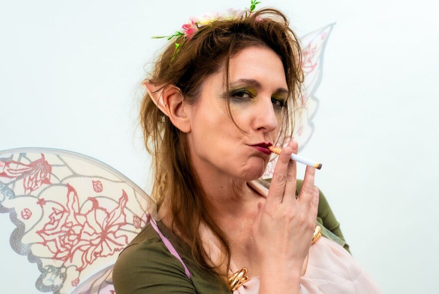 Woman dressed as a fairy smoking a cigarette and looking dishevelled.