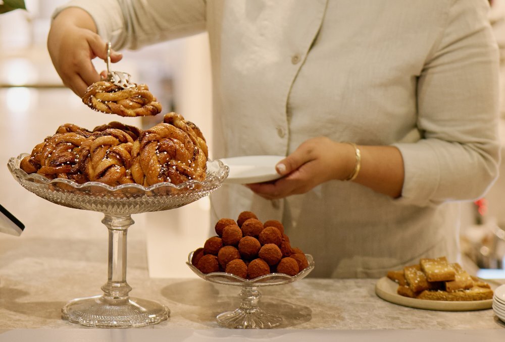 Some taking a cinnamon bun from a glass stand in a cafe.