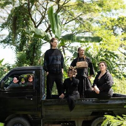 People on the back of a flatbed truck in a tree and fern setting.