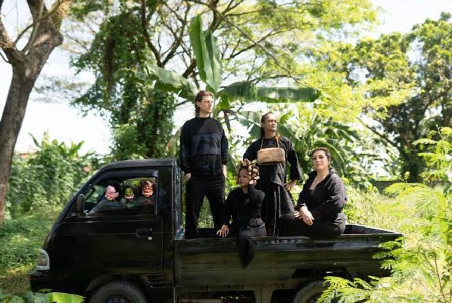 People on the back of a flatbed truck in a tree and fern setting.