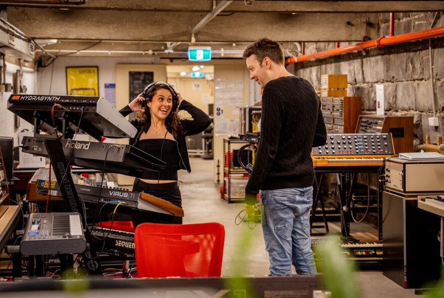 Two people in a studio that is filled with electronic music equipment and instruments.