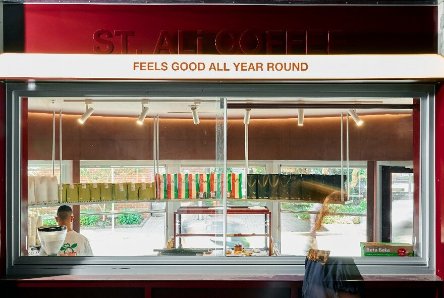 Looking through a rear window into the interior of the St ALi coffee kiosk at University of Melbourne showing the top half of a person working making coffees in the space.