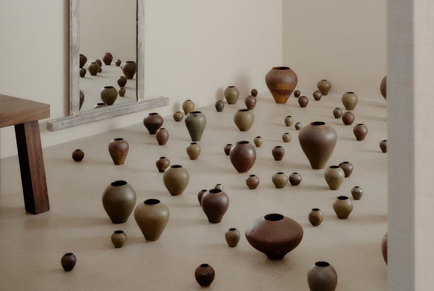 A cream-coloured gallery space with varying sizes of small wooden pots displayed as though scattered on the floor.