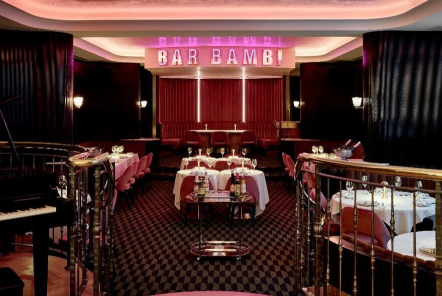 A small, red cabaret lounge with tables set and a stage that reads BAR BAMBI