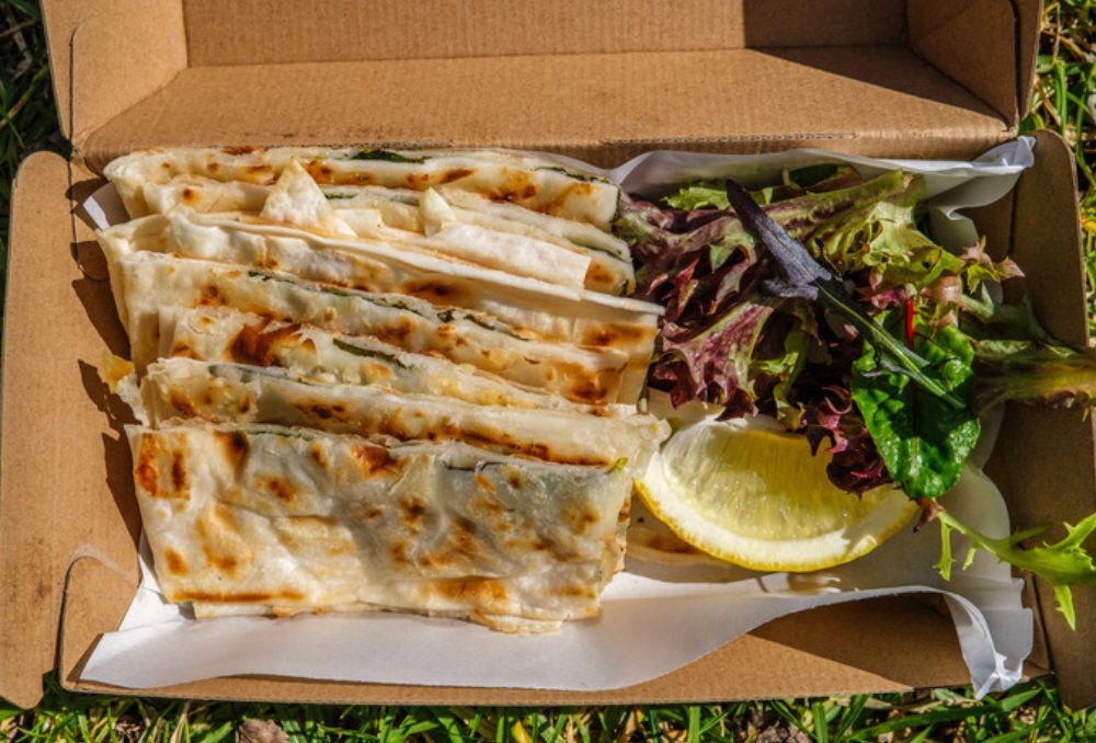 Birds-eye-view of Gozleme in a box with lettuce and lemon.