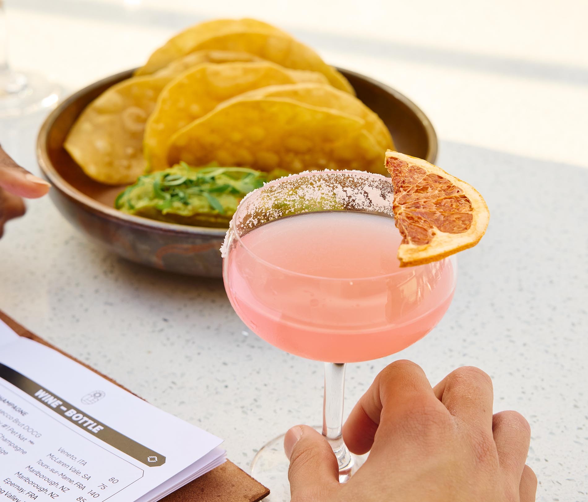 A pink margarita and guac and chips.