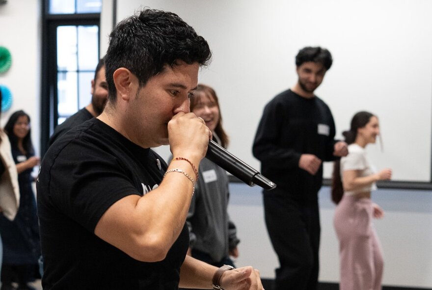 An interactive dance workshop in a studio, where participants are learning a dance following instructions from a man holding a microphone.