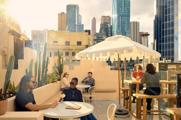 People drinking margaritas on a rooftop bar with cacti and umbrellas in the city.