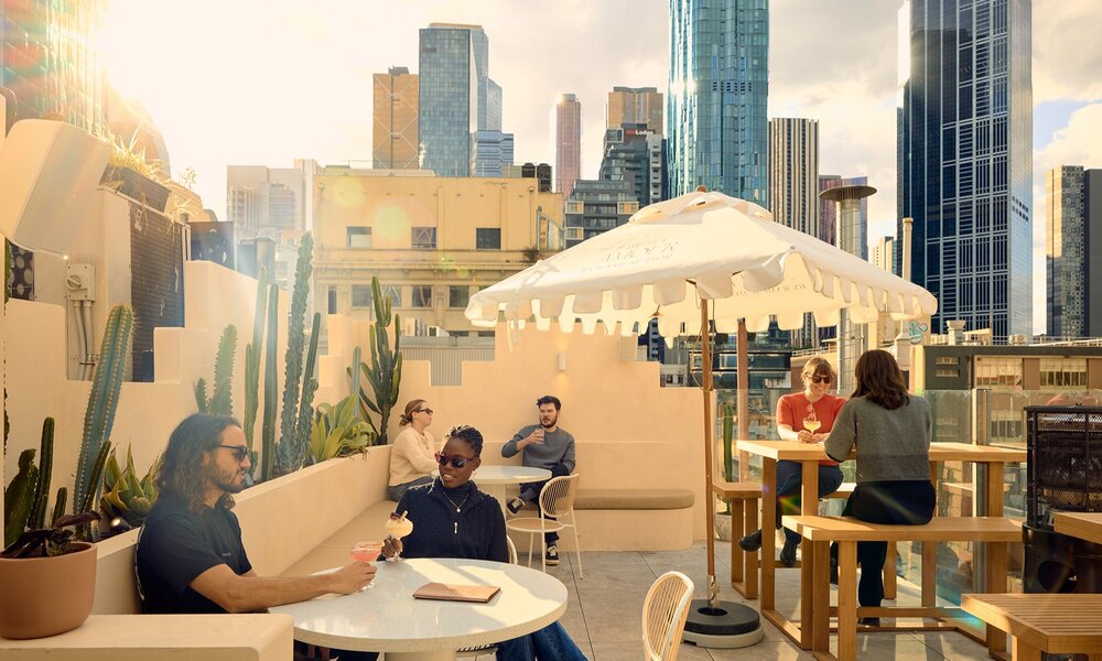 People drinking margaritas on a rooftop bar with cacti and umbrellas in the city.