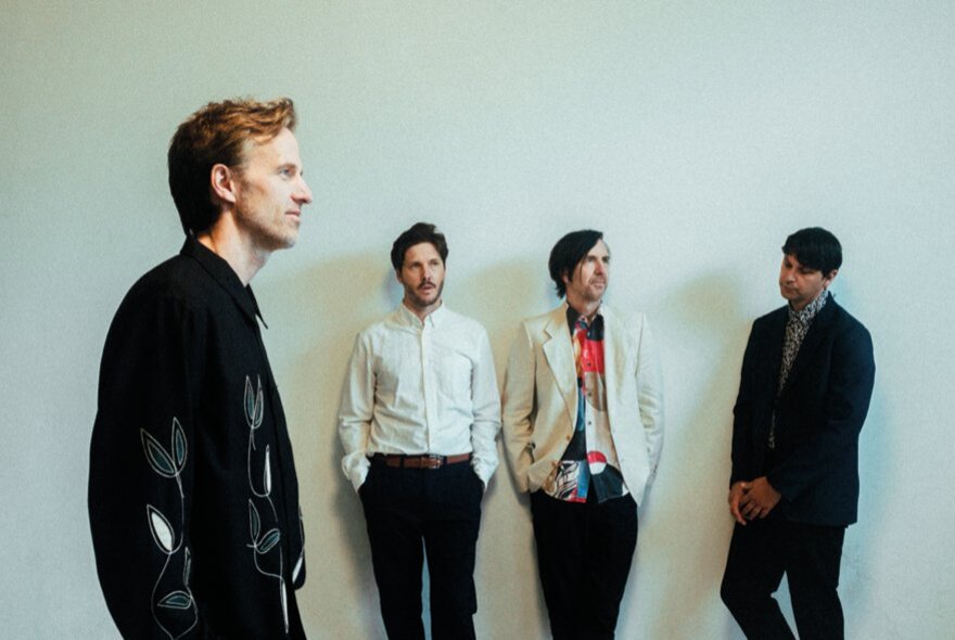 The four members of the band Cut Copy, three of them leaning against a white wall and one of them in profile in the foreground.
