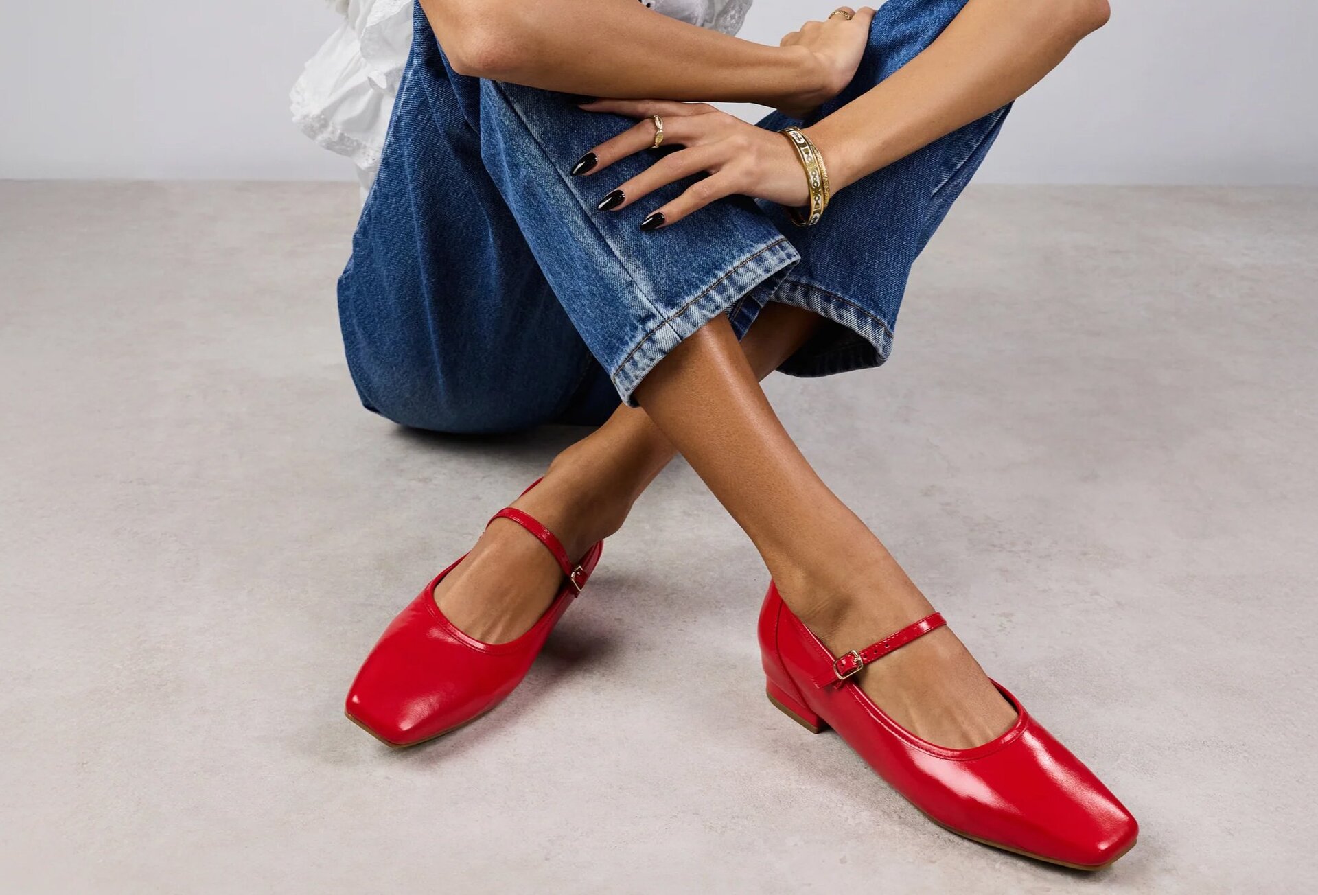 A model wearing red shiny square toe ballet flats with jeans.