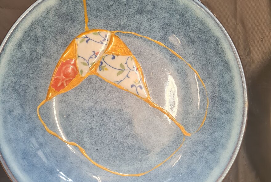 Grey plate mended with gold glue and mismatched patterned inset.