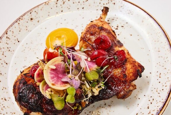 Meat with vegetable garnishes on a speckled plate.