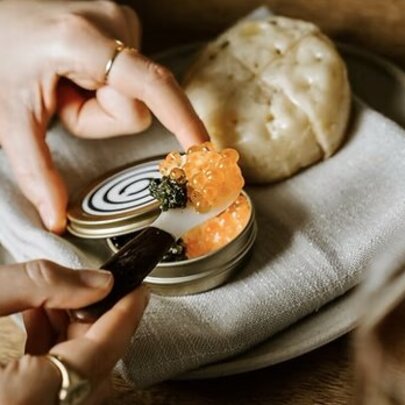 Someone scooping caviar out of a tin to put on a crumpet.
