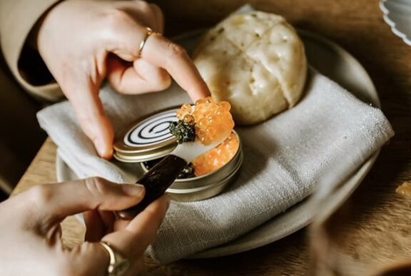 Someone scooping caviar out of a tin to put on a crumpet.