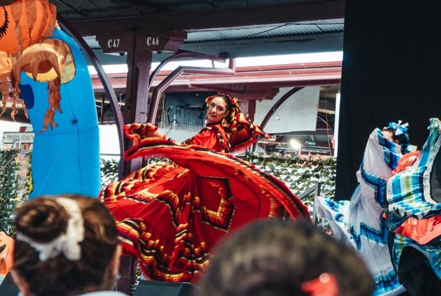 Dancers with vibrant costumes performing on stage in a market venue.