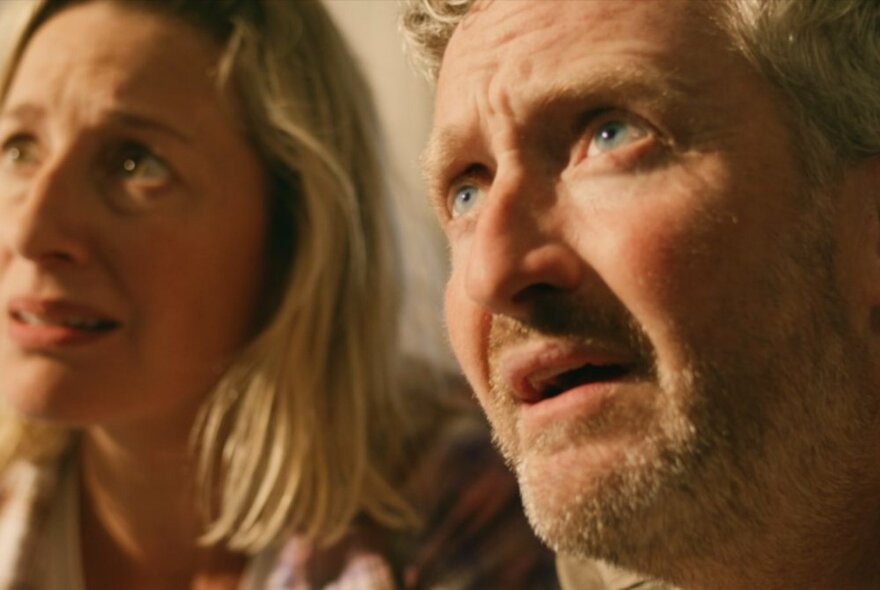 A still from an Australian movie, with a man and a woman looking up at something with distraught faces.